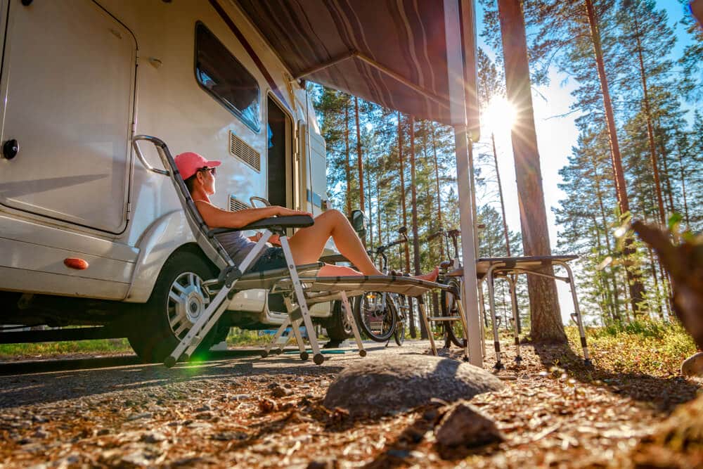 woman sitting in a lawnchair under an RV camper awning in the woods