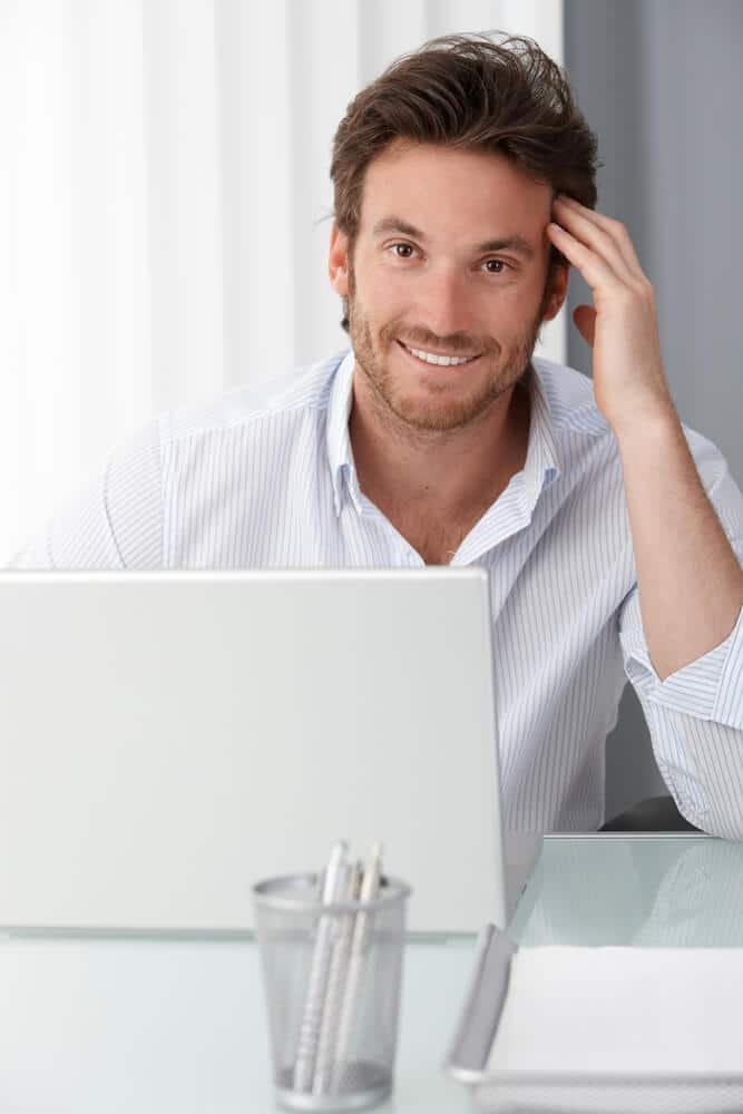 Man Smiling While Working on a Laptop